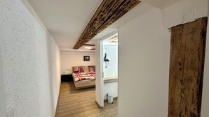 A narrow hallway leading to a bedroom with a wooden ceiling, a bed with a patterned bedspread, and a small window with a curtain. - 2-room apartment in prime city center location with terrace & DreiWelten-Card (Bad Dürrheim)