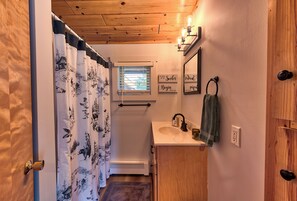 A bathroom with a wooden ceiling, a window with blinds, a sink with a towel, and a mirror with a sign above it. - Anni's Cottage, Free Wi-Fi and Air Conditioning (Indian River)