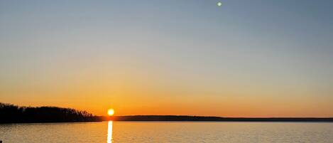 Auringonlasku tyynen vesistön yllä, kauempana näkyy rantaviiva.