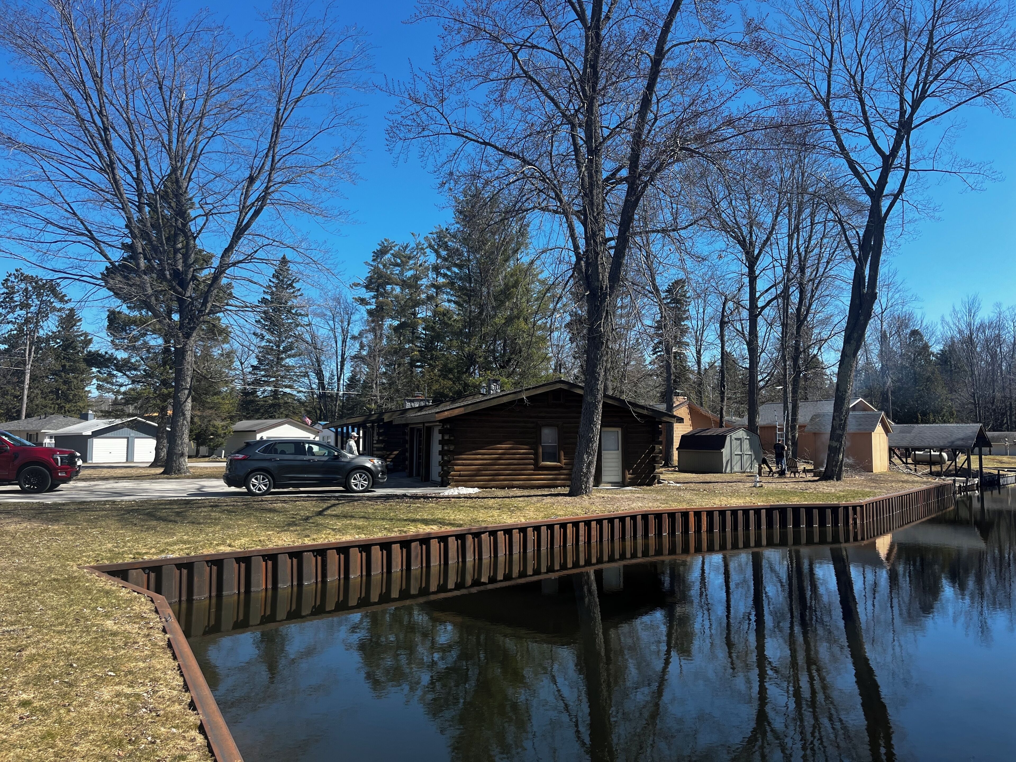 A cabin with a dock extending into a calm body of water, surrounded by trees and a clear sky.