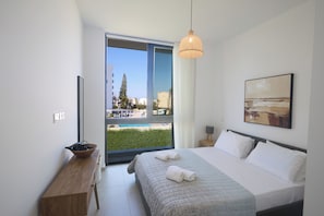 A modern hotel room with a large bed, a wooden side table, a view of a pool, and a cityscape through the window.