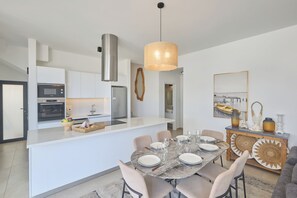 Een moderne keuken met witte kasten, een centraal eiland en een eethoek met een marmeren tafel en stoelen.