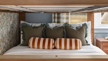 A bed with striped pillows and ruffled edges, a patterned wall, and a window with curtains.
