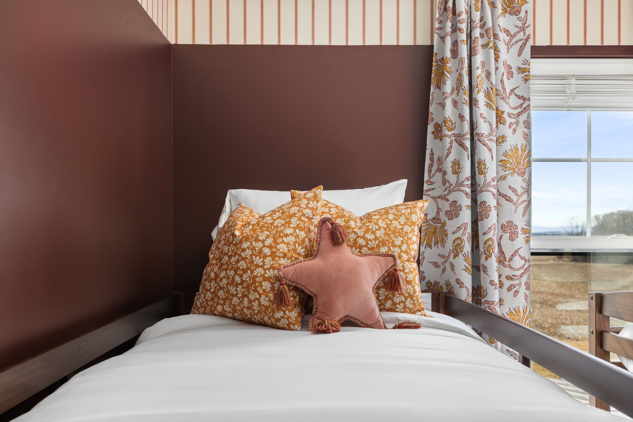 Een bed met wit beddengoed, een bruin hoofdbord en kussens met een bloemenprint.