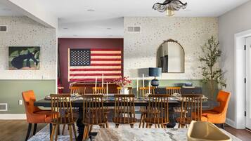 A dining area with a table set for six, surrounded by wooden chairs. An American flag is displayed on the wall behind the table.