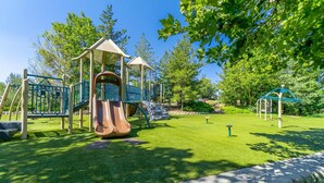 A playground with a slide and climbing structures, surrounded by green grass and trees. - Modern 3-bedroom Escape in Northwest Reno (Reno)