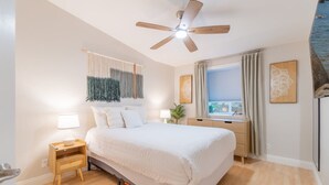 A bedroom with a bed, bedside tables, a ceiling fan, a window with curtains, and artwork on the walls. - Modern 3-bedroom Escape in Northwest Reno (Reno)