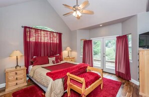 A bedroom with a bed, two nightstands, a ceiling fan, and a large window with curtains.