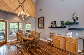 A dining area with a wooden table and chairs, a chandelier, and a kitchen with wooden cabinets and a countertop.