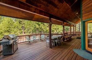 A wooden deck with a grill, outdoor seating, and a view of the forest.