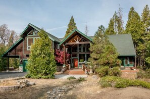A two-story log cabin with a green roof, a front porch, and a stone foundation.