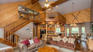 A spacious living area with a high ceiling, wooden staircase, and a cozy seating arrangement. - Handels Pride- Family friendly, Game Room & Views (Shaver Lake)