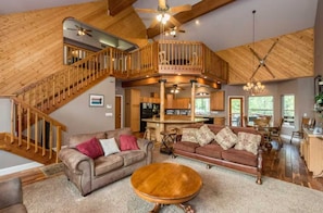 A spacious living area with a high ceiling, wooden staircase, and a cozy seating arrangement.