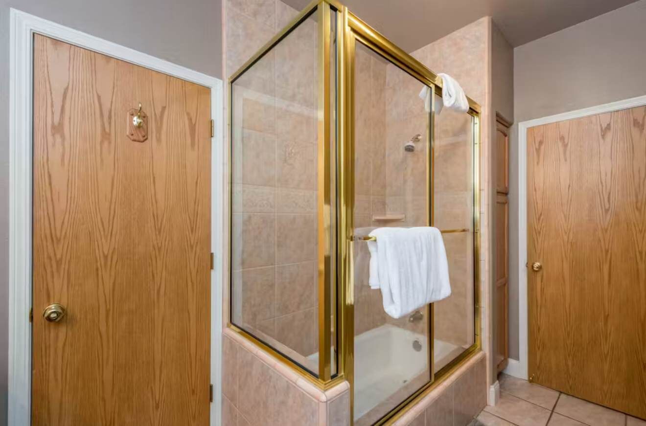 A bathroom with a glass-enclosed shower, wooden doors, and a white towel hanging on the shower door.