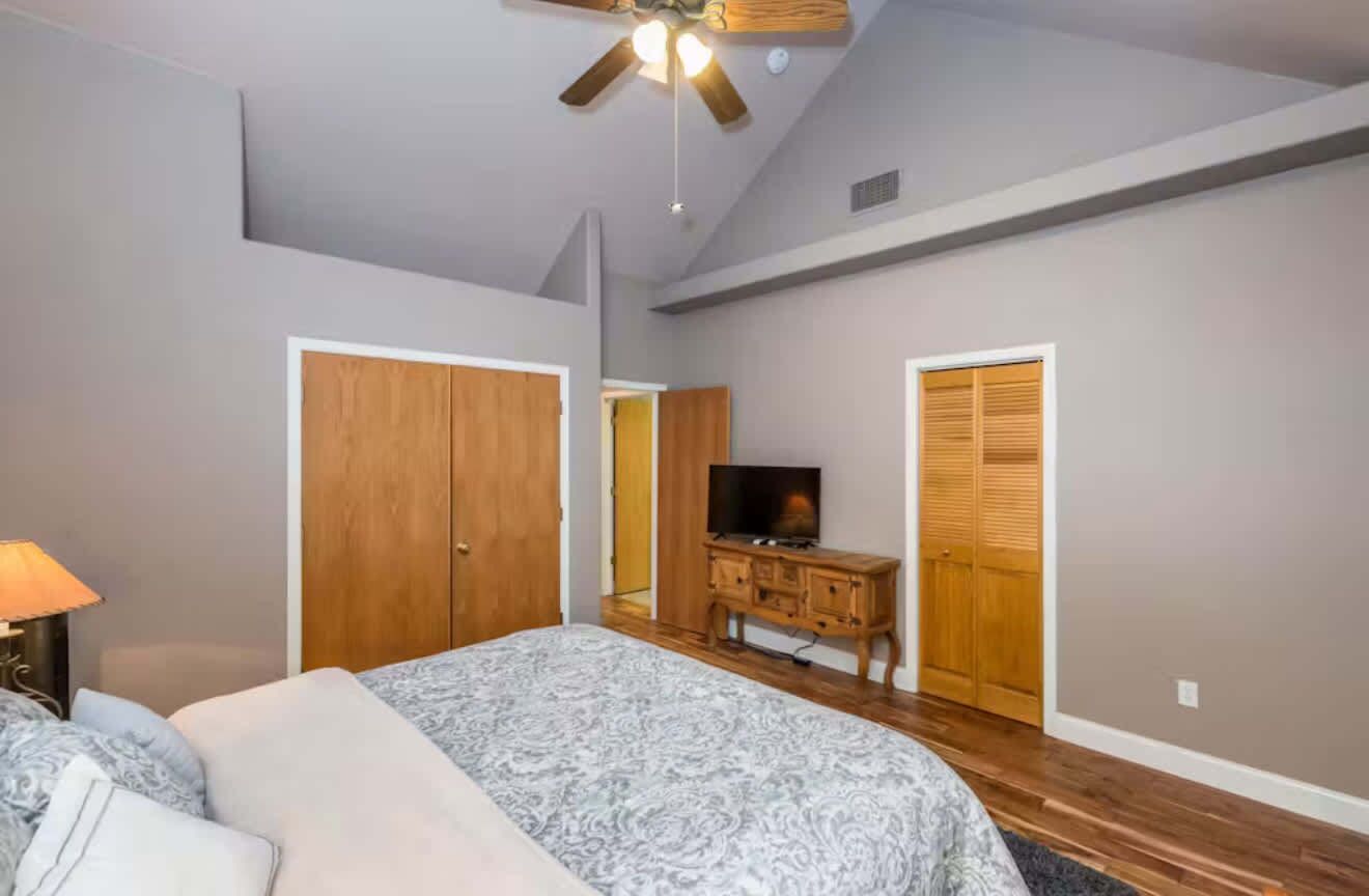 A bedroom with a bed, a wooden wardrobe, a television, and a ceiling fan.