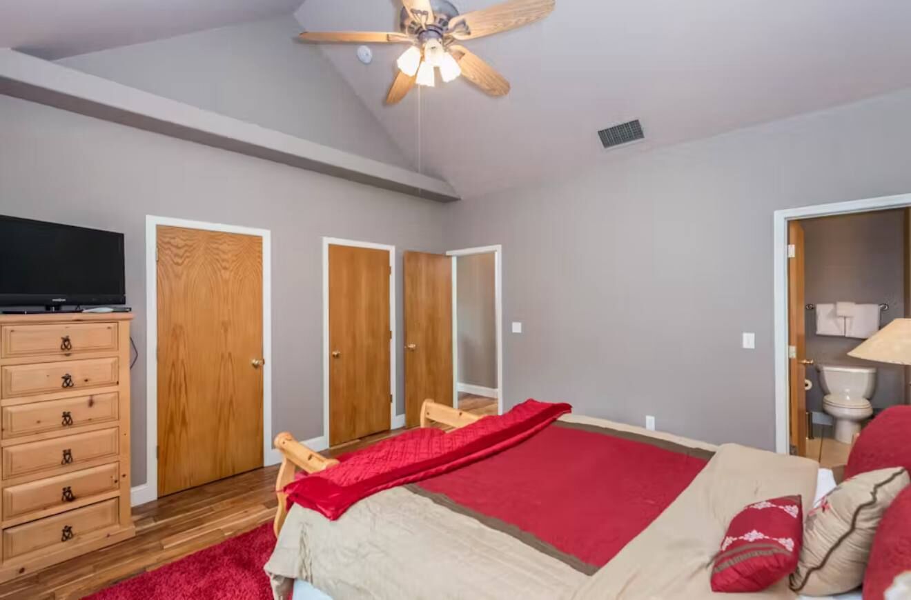 A bedroom with a bed, a ceiling fan, a dresser, and a television.