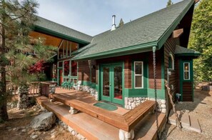 A log cabin with a green roof, stone foundation, and a wooden deck.