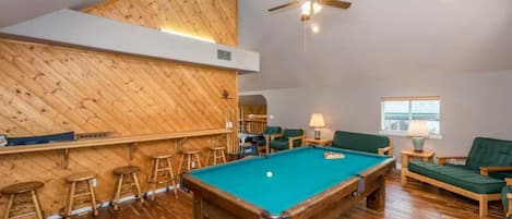 A pool table in a room with wooden flooring and a sloped ceiling.