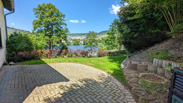 Eine gepflasterte Terrasse mit Blick auf einen See und Hügel im Hintergrund.