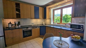 Eine moderne Küche mit Holzschränken, einem eingebauten Ofen, einer Mikrowelle und einem großen Fenster mit Blick auf Grünflächen.