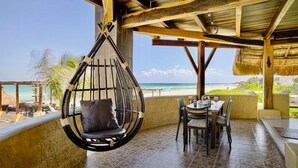 A hanging chair with a cushion, a table with chairs, and a view of the beach.