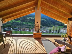 Una terraza de madera con vistas a un valle, una mesa, sillas y un banco.