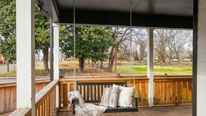 Eine überdachte Veranda mit einer Holzschaukel, einer Bank und Blick auf einen Park.