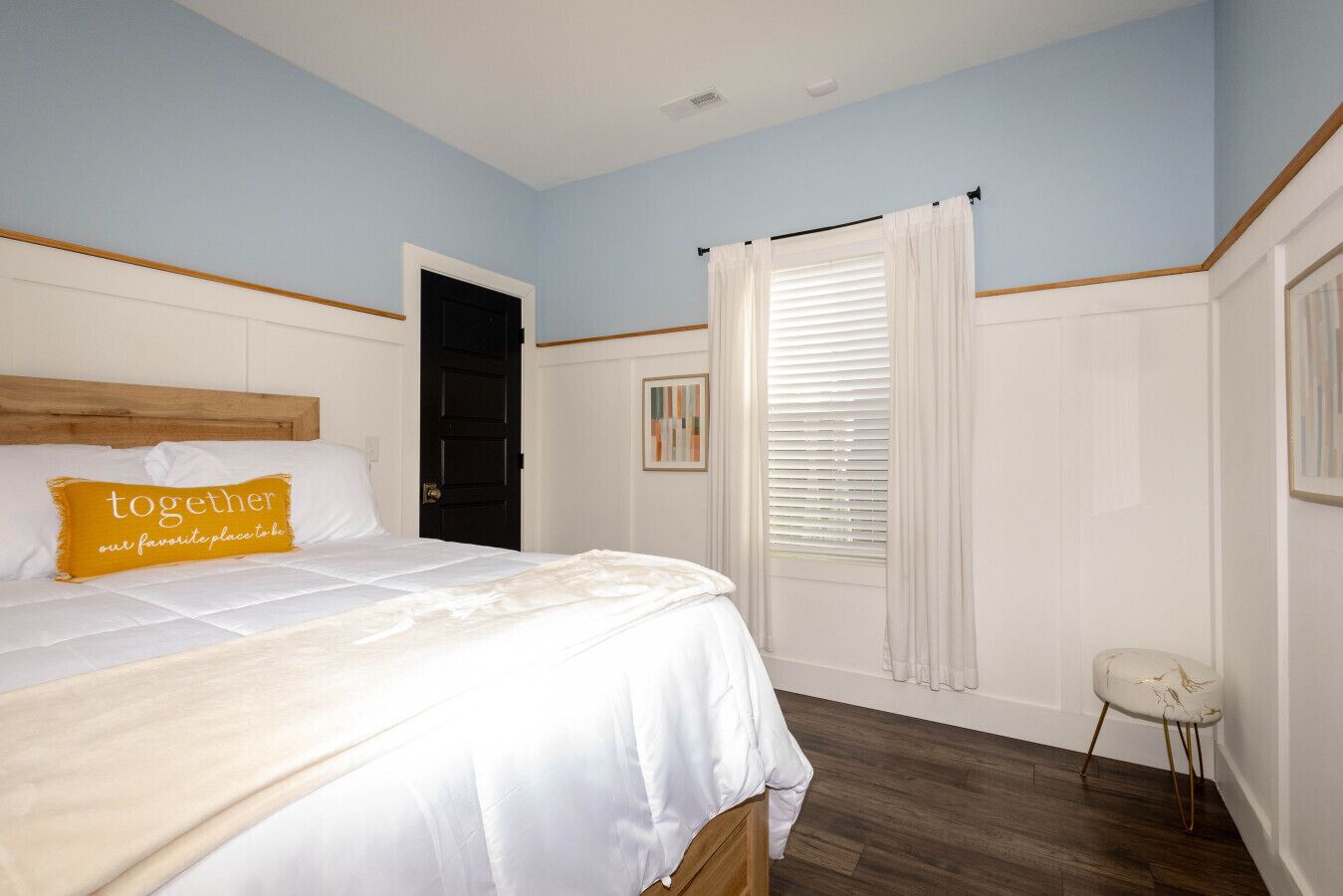 A bedroom with a bed, a door, a window with curtains, and a small stool.