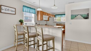 A kitchen with wooden cabinets, a white refrigerator, and a bar area with two stools.