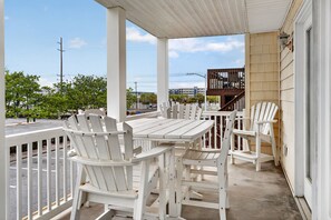 A covered outdoor area with a table and chairs, a wooden fence, and a view of the street and buildings in the background. - Spacious 3-Bedroom Ocean Block Townhome – Steps from the Sand! (Ocean City)