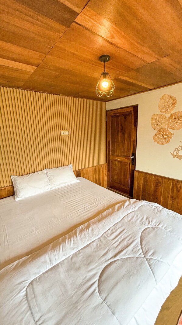 A room with a wooden ceiling, a bed with white bedding, a wooden door, and a wall with leaf patterns.