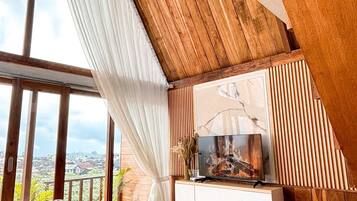 Ein modernes Wohnzimmer mit hohen Decken, Holzbalken, einem großen Fenster mit Vorhängen, einer Couch und einem flachbildfernseher, der an einer Holzwand angebracht ist.