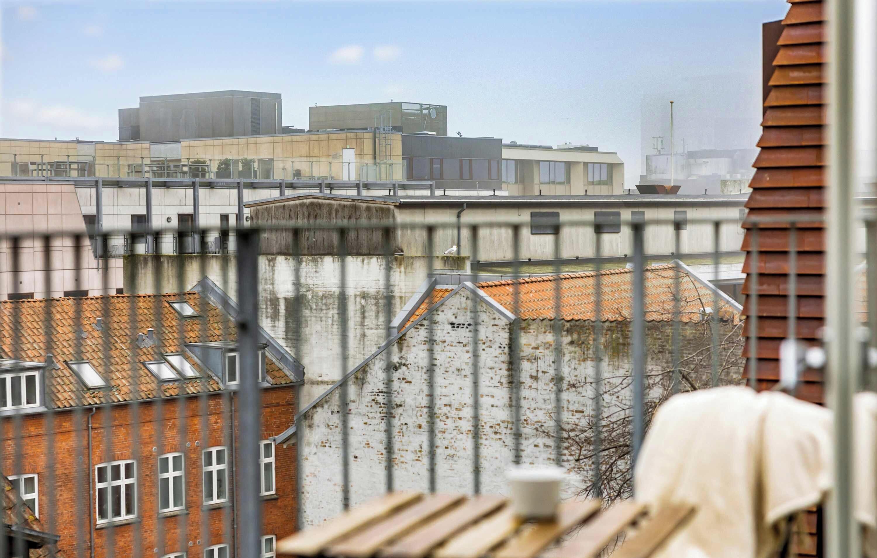 Uitzicht op een stadsgezicht met gebouwen, een metalen hek en een houten tafel met een kopje.