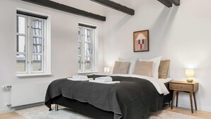 Un dormitorio con cama, mesitas de noche, un radiador y ventanas.