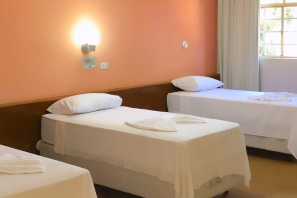 Ein Hotelzimmer mit zwei Einzelbetten, einem Holzkopfteil, einem Lichtschalter und einem Fenster mit Vorhängen.