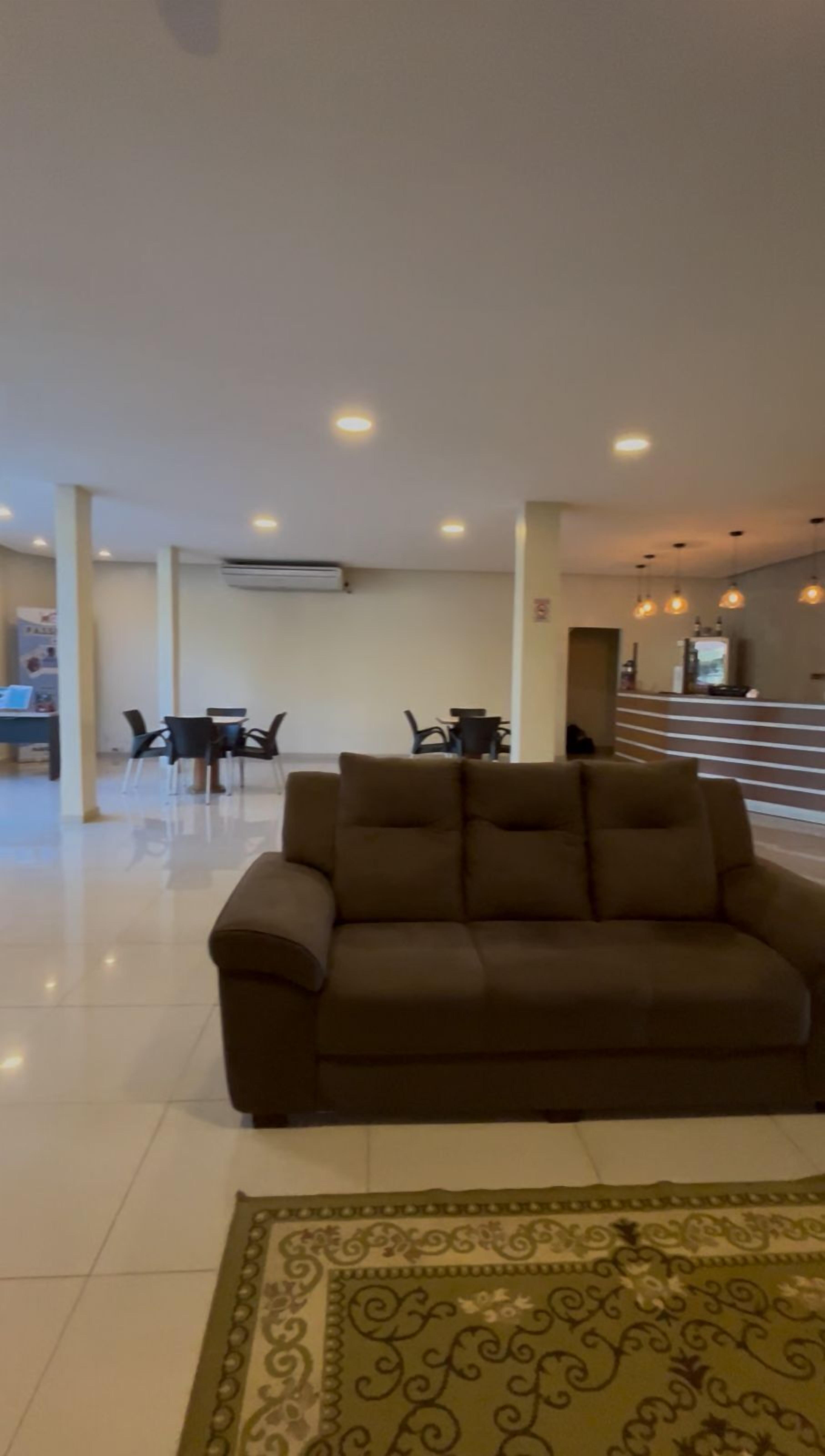 A spacious living area with a brown sofa, a dining table with chairs, and a patterned rug.