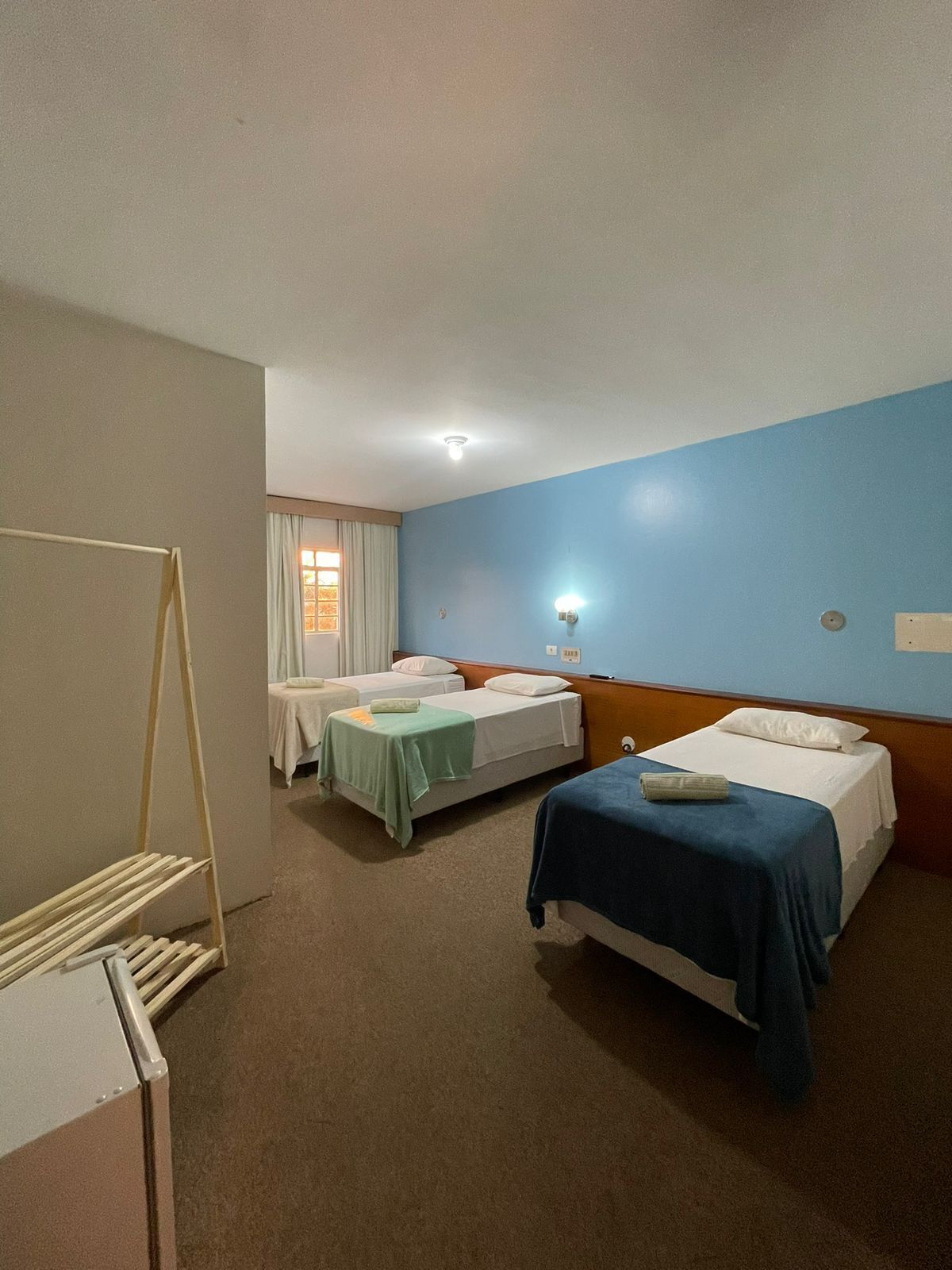 Habitación de hotel con dos camas, una mesita, un tendedero y una ventana con cortinas.