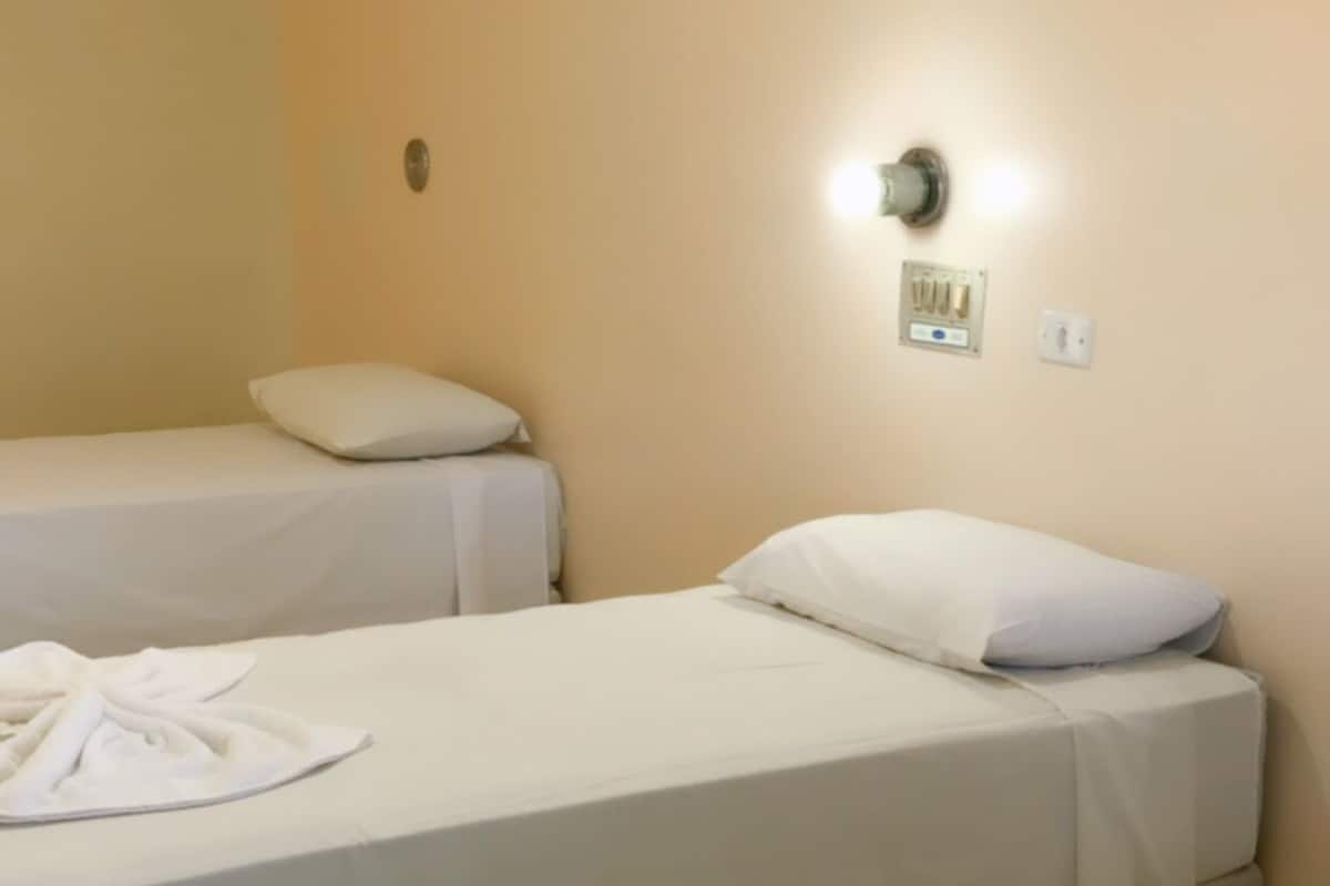 Ein Hotelzimmer mit zwei Einzelbetten, jeweils mit einem weißen Kopfkissen und einem ordentlich gefalteten weißen Handtuch.