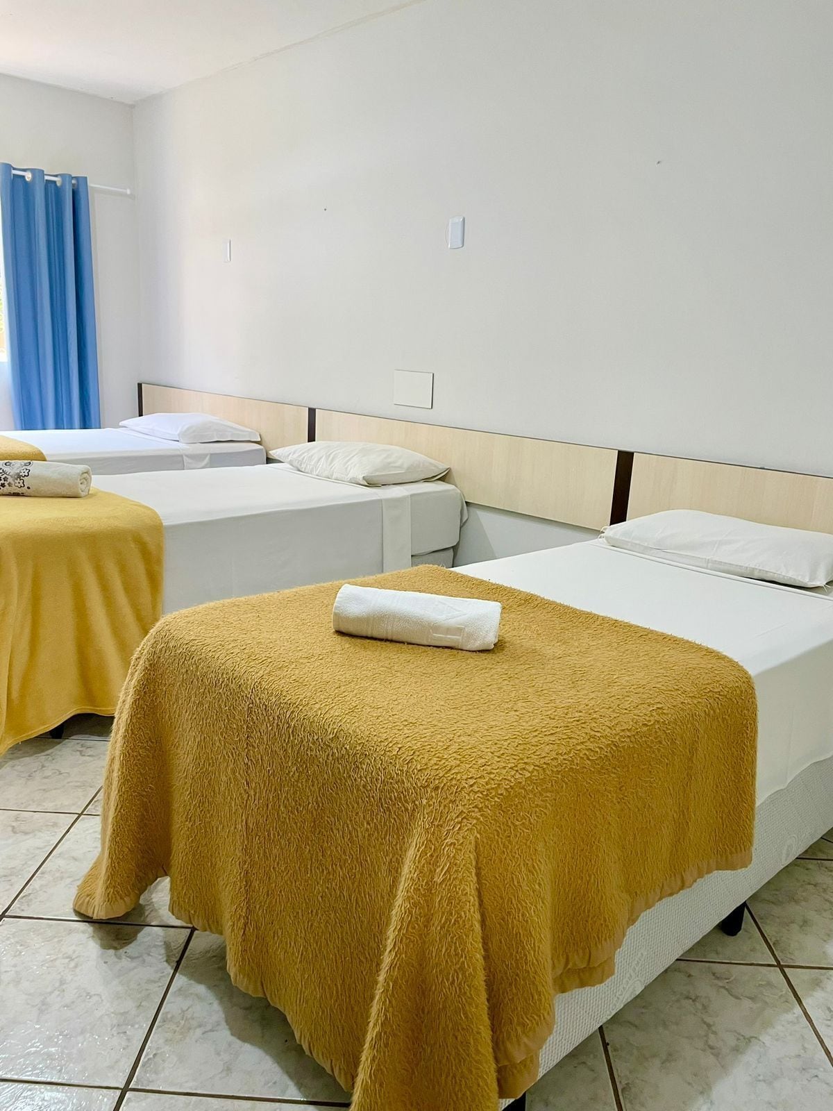 A hotel room with two beds, a blue curtain, and a tiled floor.
