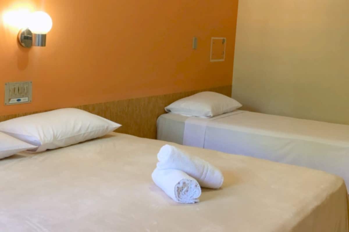 Ein Hotelzimmer mit zwei Betten, jeweils mit weißer Bettwäsche und Kissen, sowie einer Wandleuchte.