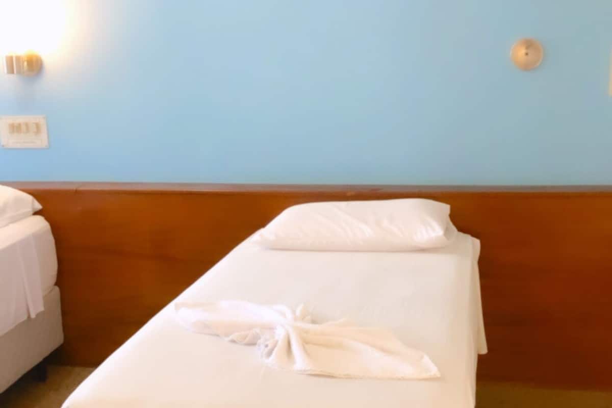 Ein Einzelbett mit weißen Leinentüchern und einem Handtuch, eine hellblaue Wand und ein Holz-Kopfstück.