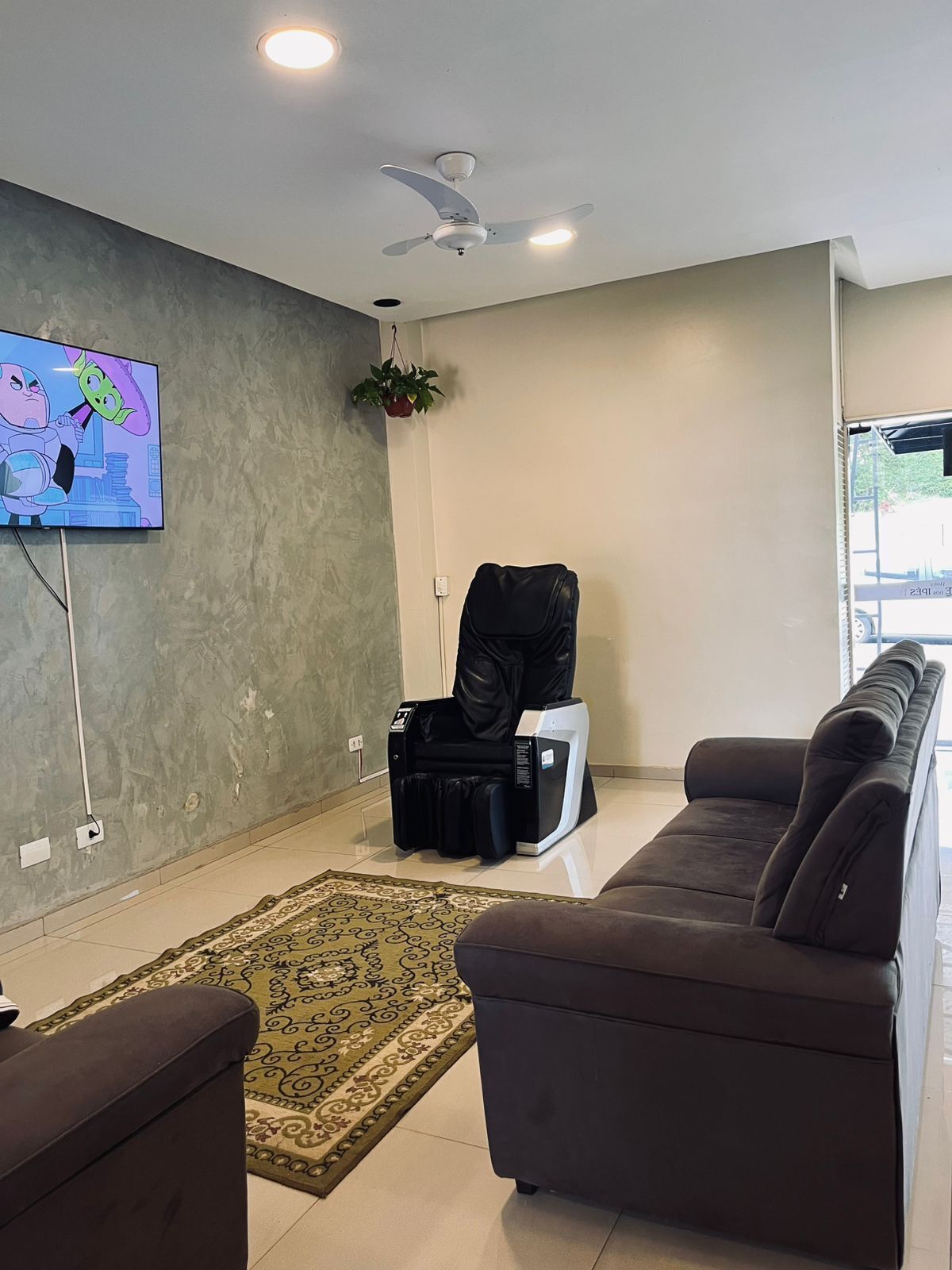 A living room with a sofa, a television, a ceiling fan, a small plant, and a luggage trolley.