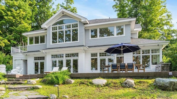 Une maison à deux étages dotée d’une grande terrasse, d’un espace salon extérieur et d’un jardin bien entretenu.
