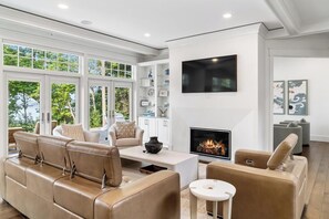 A modern living room with a fireplace, leather sofas, and a large window. - Blue Beech Estate- Beautiful Waterfront Estate! (Harbor Springs)