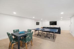 A room with a ping pong table, a sofa, and a flat-screen TV.