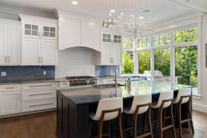 A modern kitchen with white cabinetry, a large island with bar stools, and a view of the outdoors through large windows.