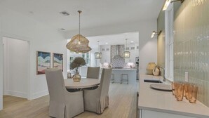 A modern kitchen with a dining area, featuring a round table with chairs, pendant lighting, and a view into the adjacent dining room. - Newly Remodeled | Watercolor Resort | Golf Cart! (Santa Rosa Beach)
