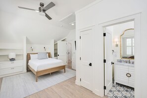 Een slaapkamer met een bed, nachtkastjes, een plafondventilator en een badkamer met een spiegel en wastafel.