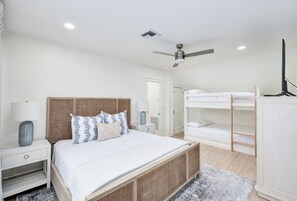 A bedroom with a bed, bedside tables, a ceiling fan, bunk beds, and a TV.