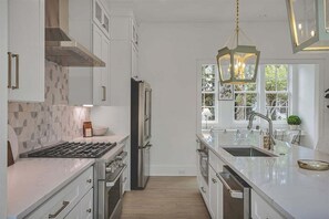 Cozinha moderna com armários brancos, eletrodomésticos de aço inoxidável e uma grande janela que oferece iluminação natural.